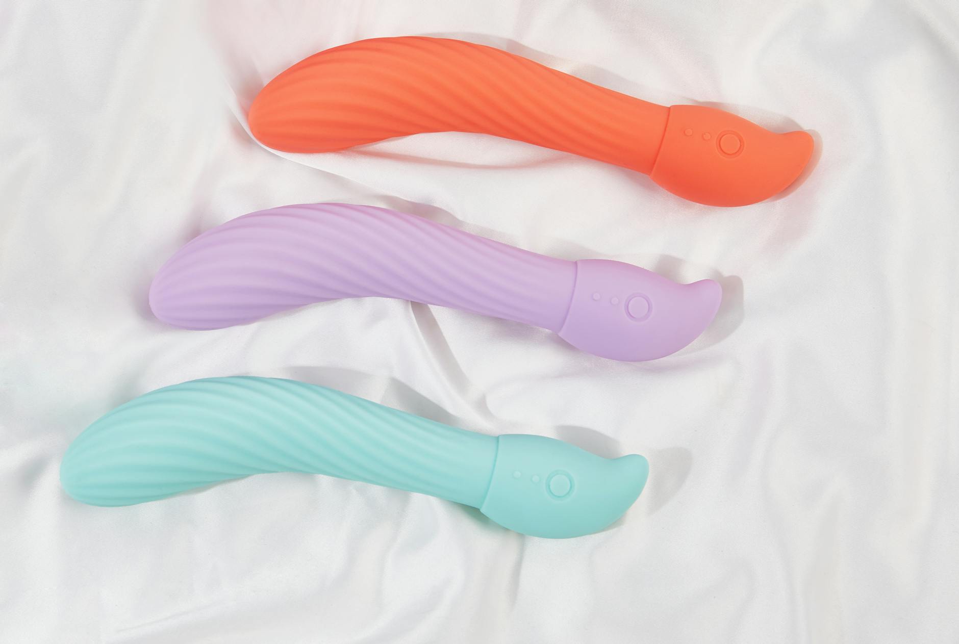 Three colorful clitoral vibrators arranged on white fabric, highlighting their smooth texture and varied stimulation options.