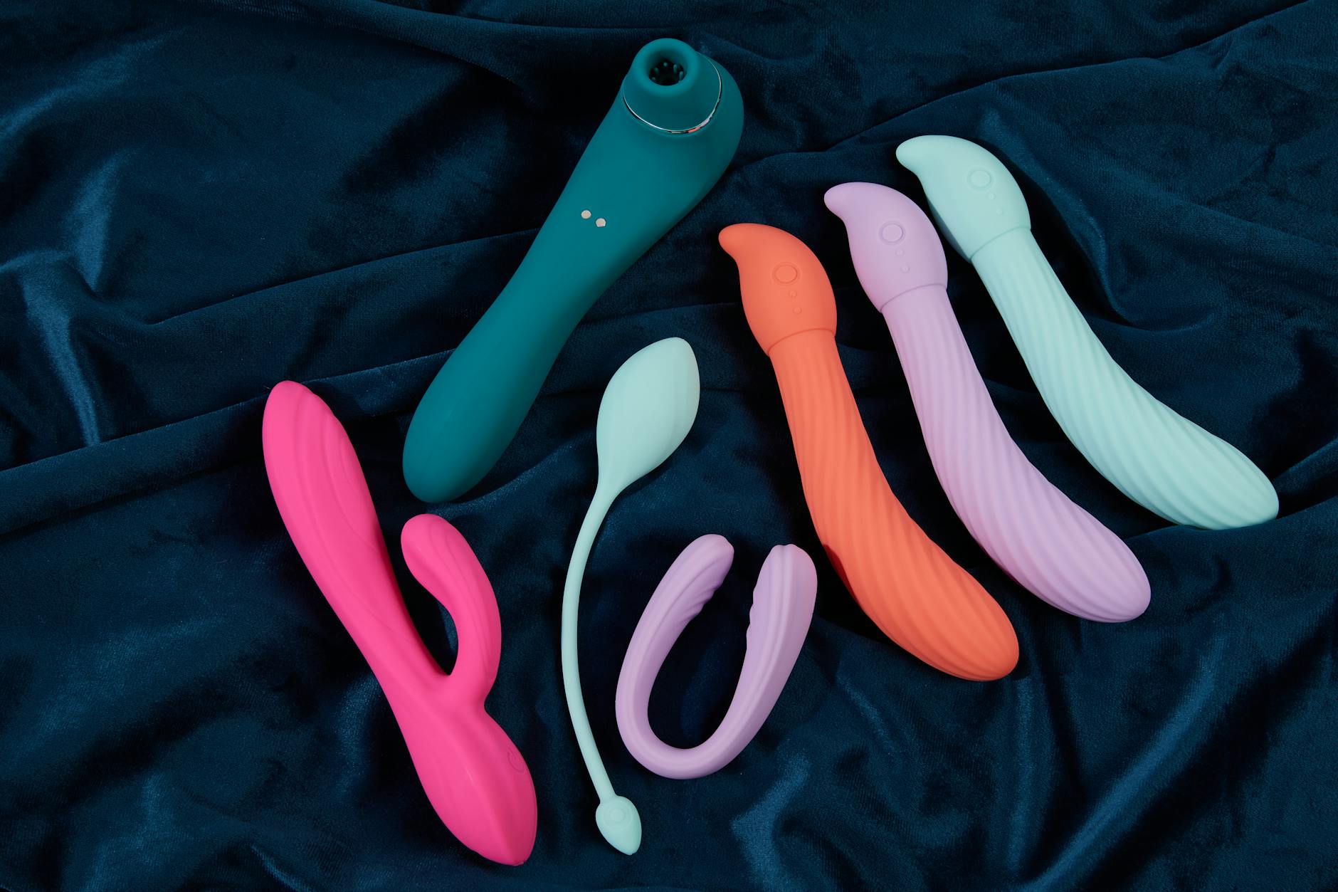 Vibradores de silicone coloridos em tecido azul escuro, mostrando várias cores e formatos