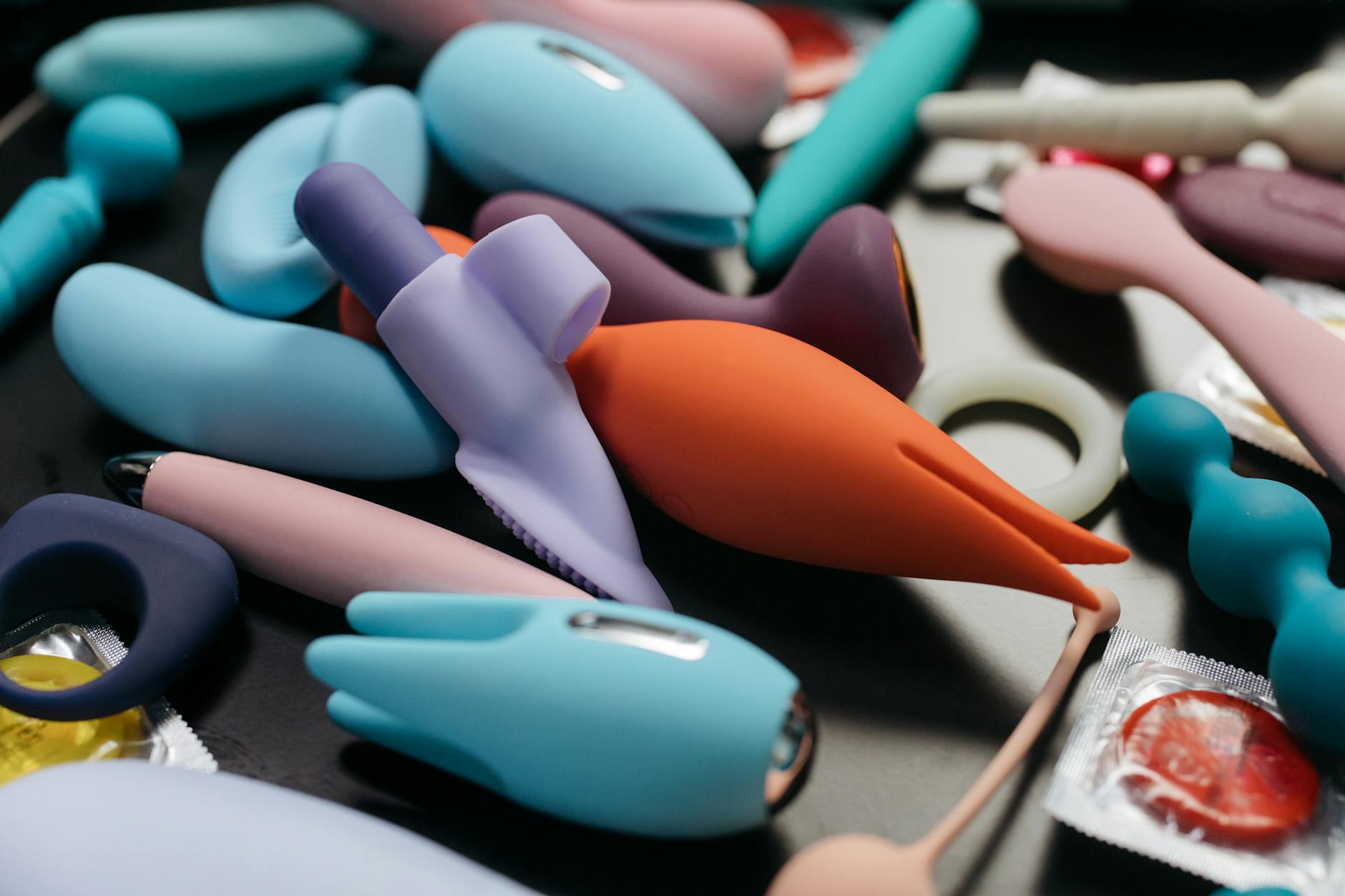 A hand reaching over a variety of colorful sex toys arranged on a table.