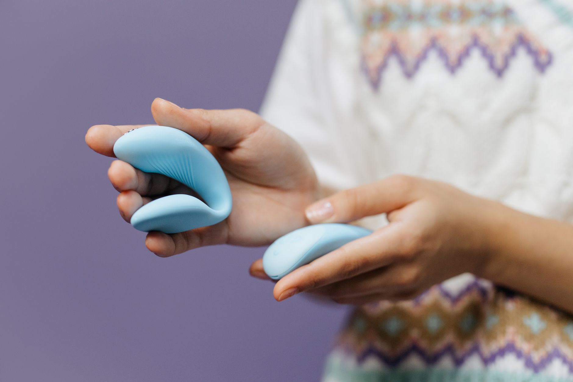 Close-up of hands holding a sleek blue vibrator, representing intimate connection and shared pleasure.