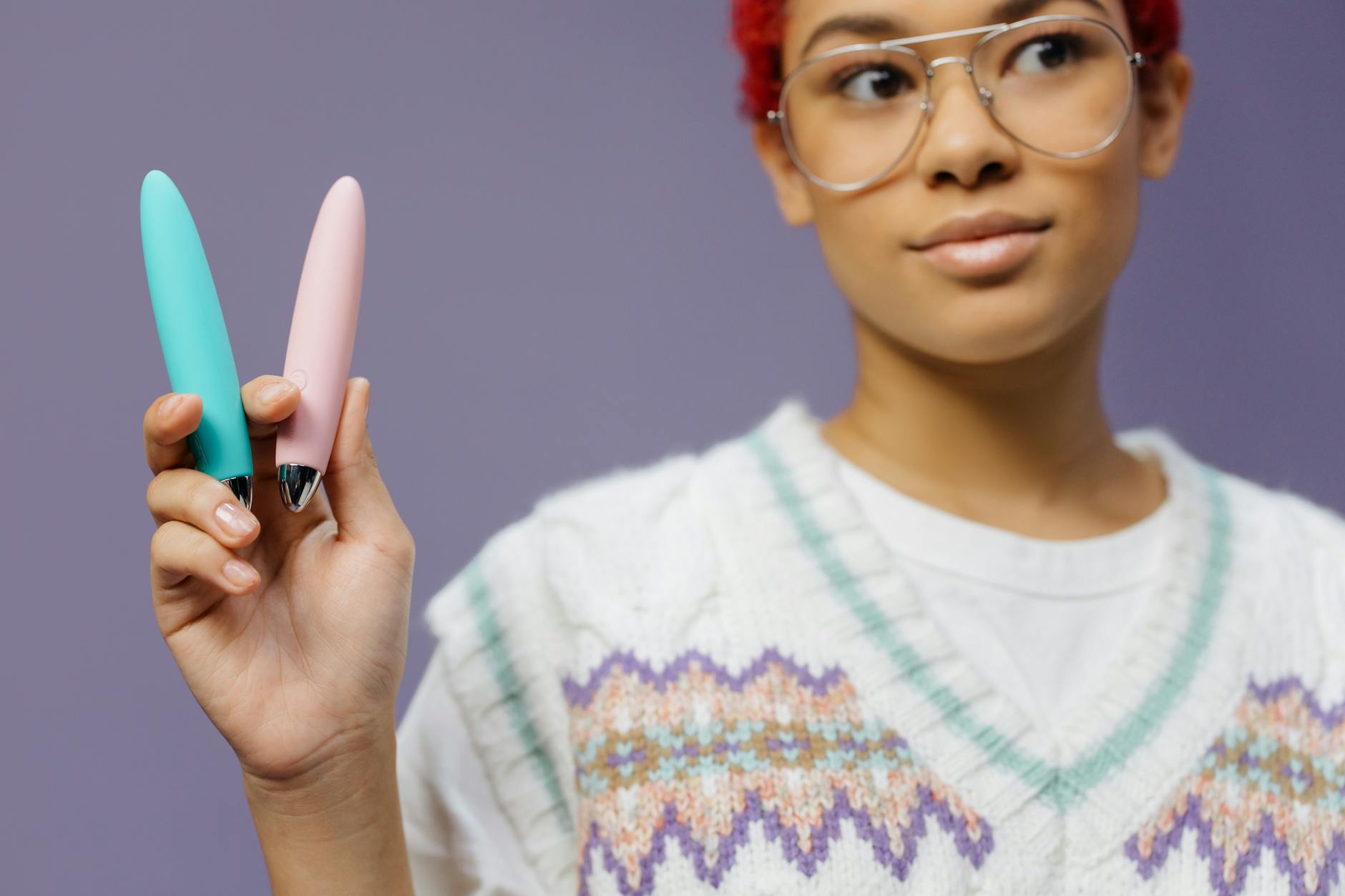 A woman holding colorful vibrators against a purple background, representing diverse pleasure tools