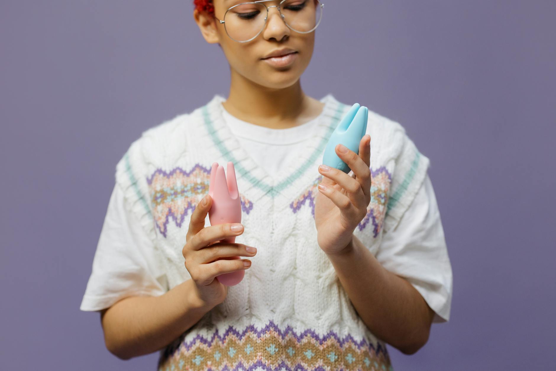 Woman thoughtfully holding blue and pink silicone vibrators, representing choice and self-exploration after menopause.